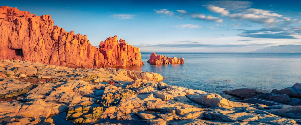 A rocky coastline with towering red rock formations and calm sea.