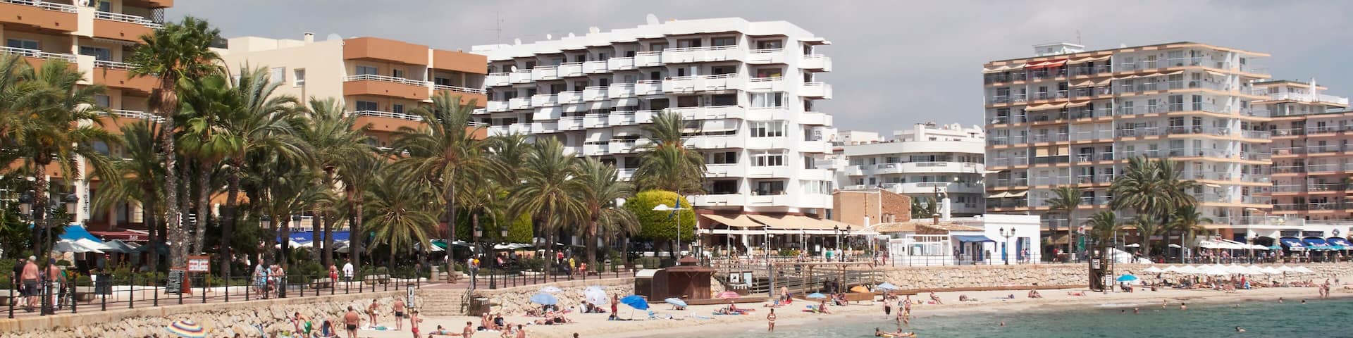 A beach with clear water, palm trees, and multi-story buildings in the background.