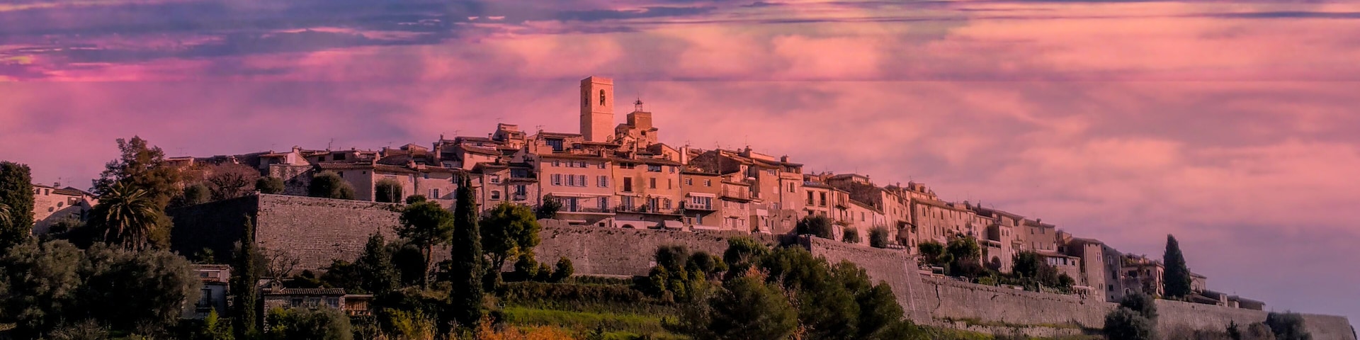 Une ville historique, perchĂ©e sur une colline et dominĂ©e par une tour imposante, entourĂ©e dâune vĂ©gĂ©tation luxuriante et offrant un panorama spectaculaire sur le ciel au coucher du soleil.