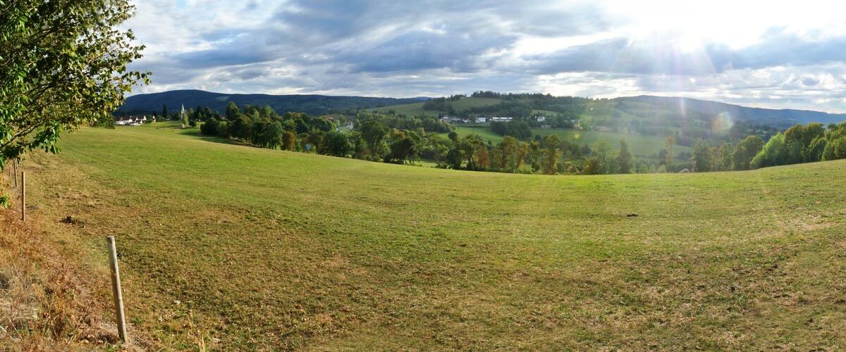 A grassy valley with a small village in the distance, surrounded by hills and trees.
