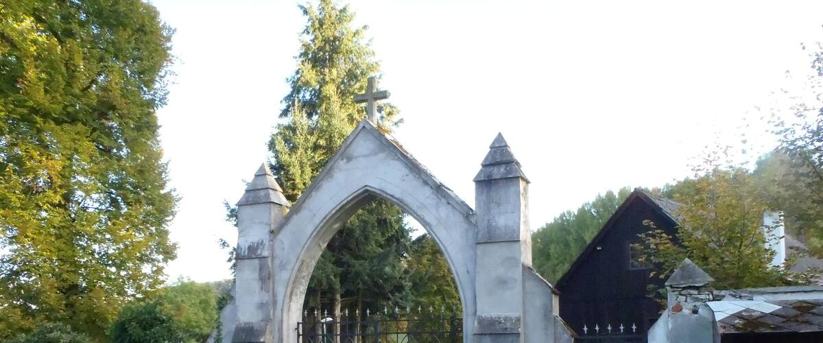 A stone archway with a cross on top, leading to a cemetery.