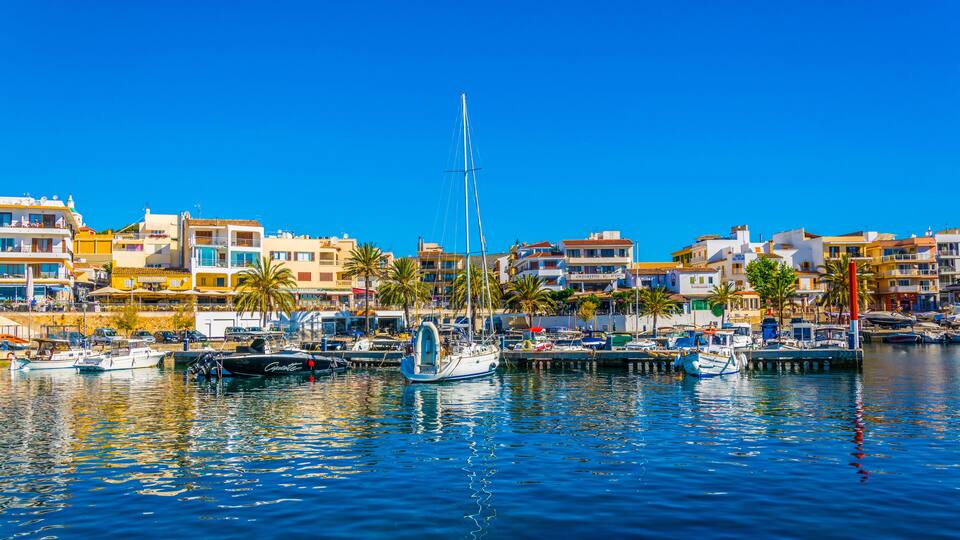 A marina with boats, a sailboat, and colorful buildings along the waterfront.