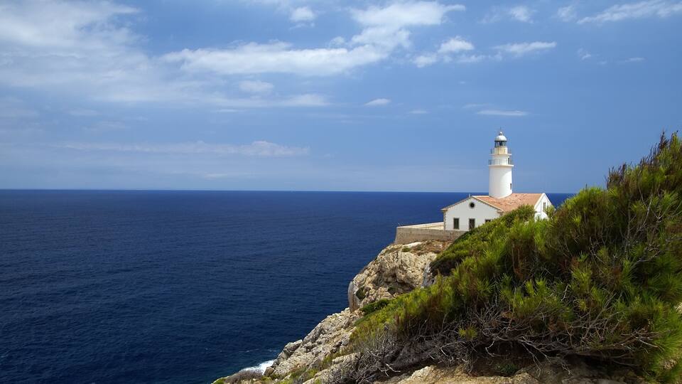 A white lighthouse on a rocky cliff overlooking the ocean.