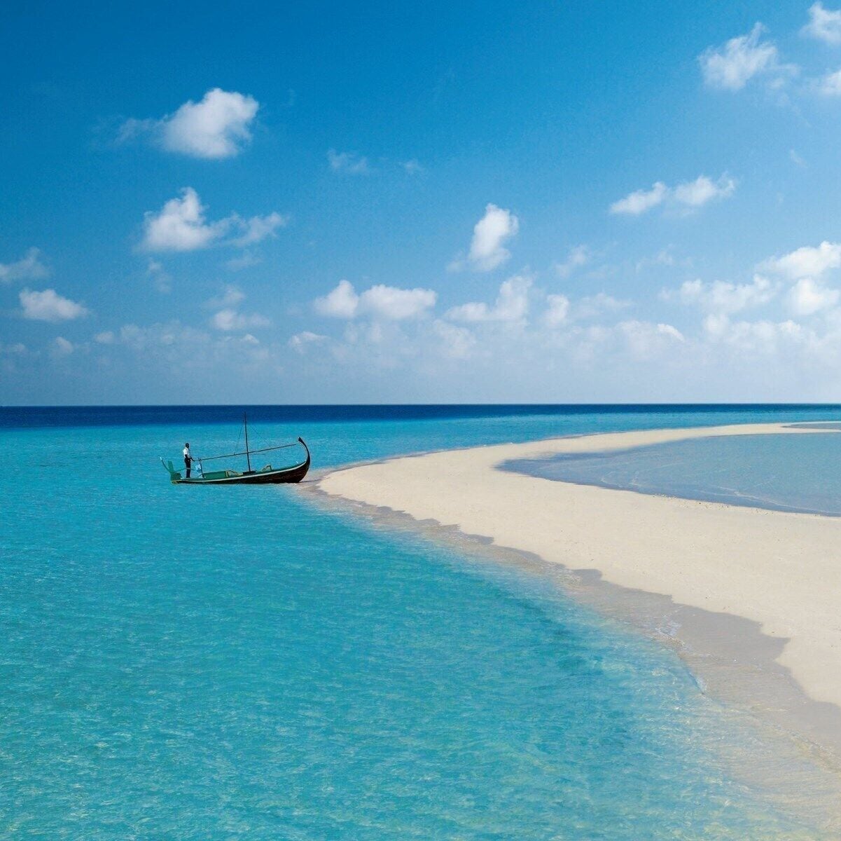 A boat on turquoise water near a white sandy beach under a clear blue sky.