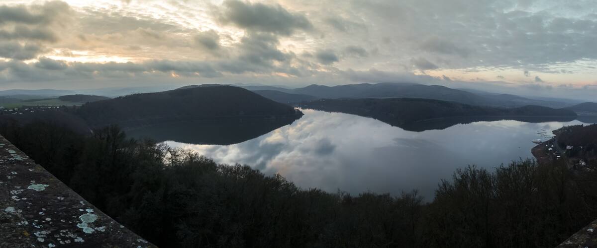 A valley with a lake surrounded by mountains and a cloudy sky.