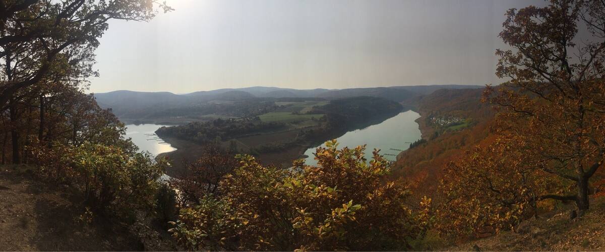 A valley with a river, surrounded by hills and autumn foliage.