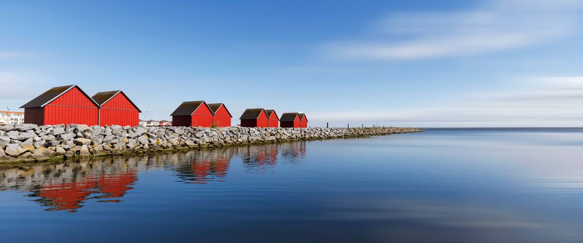 A row of red buildings by a calm body of water with a clear sky.