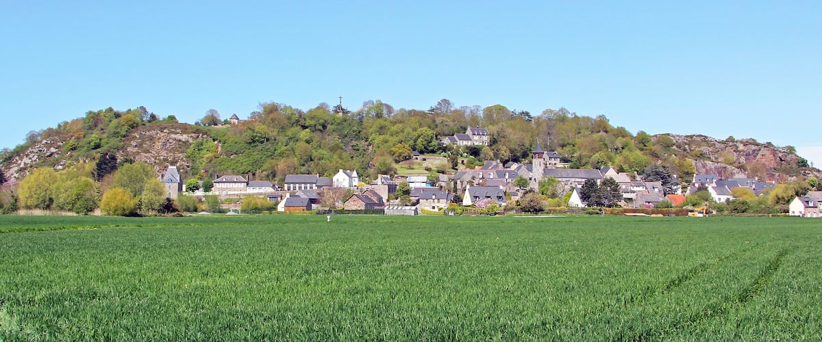 A village with houses on a hill, a green field in the foreground, and a clear blue sky.