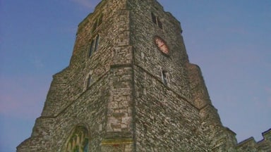 A historic stone tower with a clock and a weather vane.