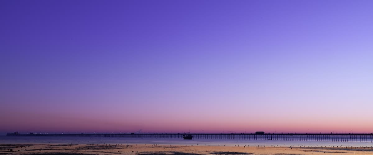 A beach at sunset with a pier extending into the water.