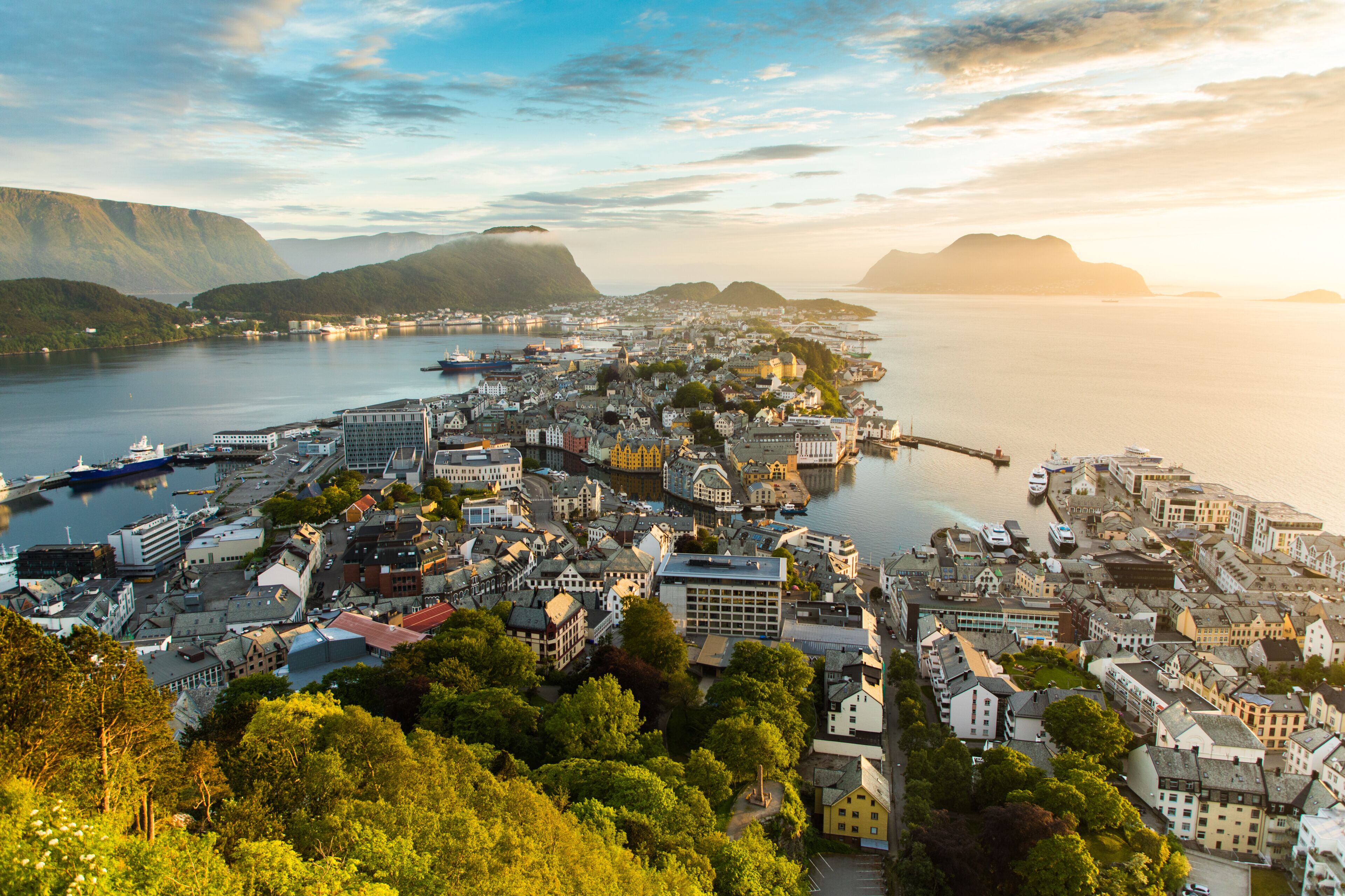 A coastal town with a harbor, buildings, and mountains in the background.