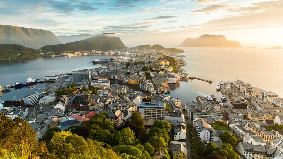 A coastal town with a harbor, buildings, and mountains in the background.