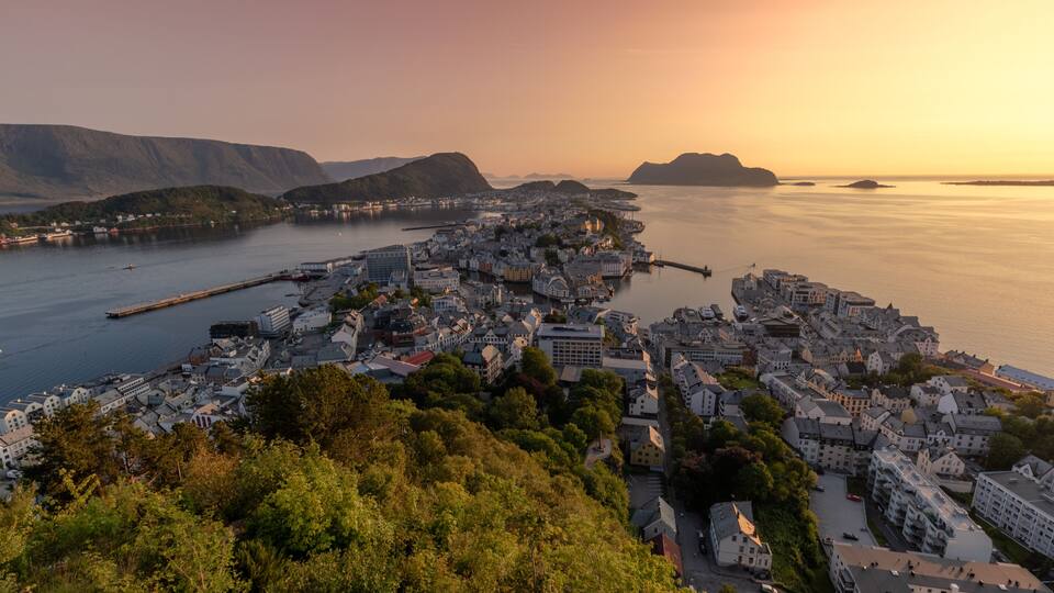 A coastal town with a harbor, surrounded by hills and dense greenery.
