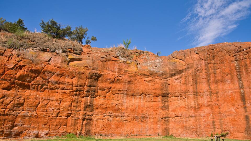 A red rock cliff with sparse vegetation and a clear blue sky.