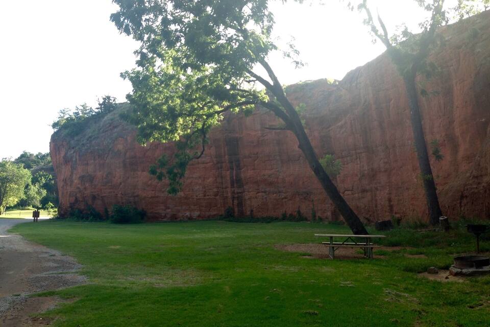 A park with a large rock formation, a grassy area, and a picnic table.