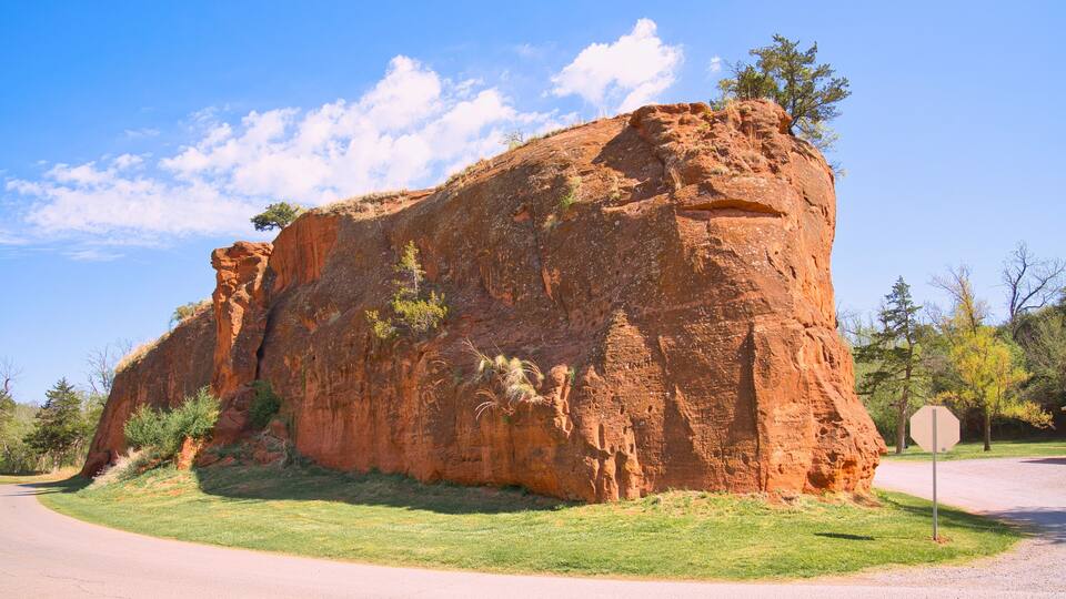 A large red rock formation with a grassy foreground and a clear blue sky.