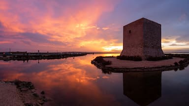 Una torre de piedra junto a un cuerpo de agua tranquilo, con el reflejo de la puesta de sol.