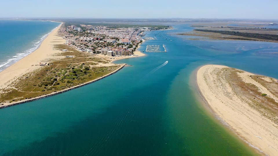 An aerial view of a coastal city with a beach, marina, and clear blue waters.