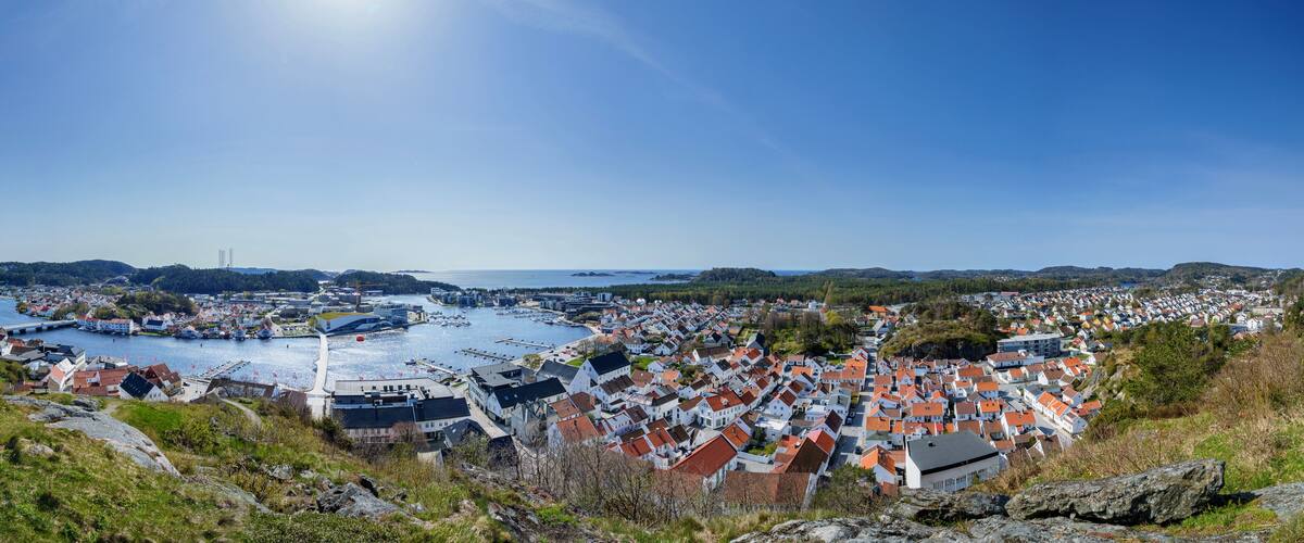 A coastal town with a marina, surrounded by hills and houses with red roofs.