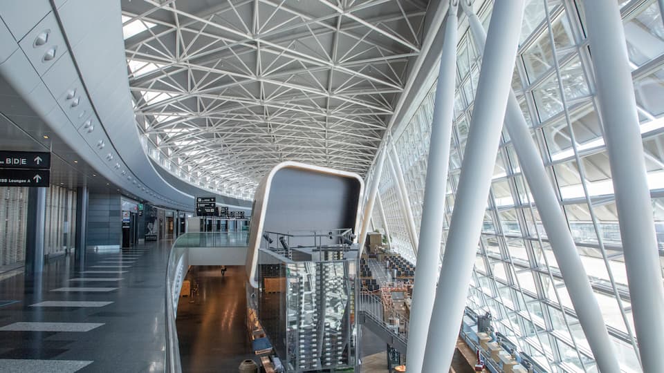 A modern airport interior with a high ceiling, glass railings, and an escalator.