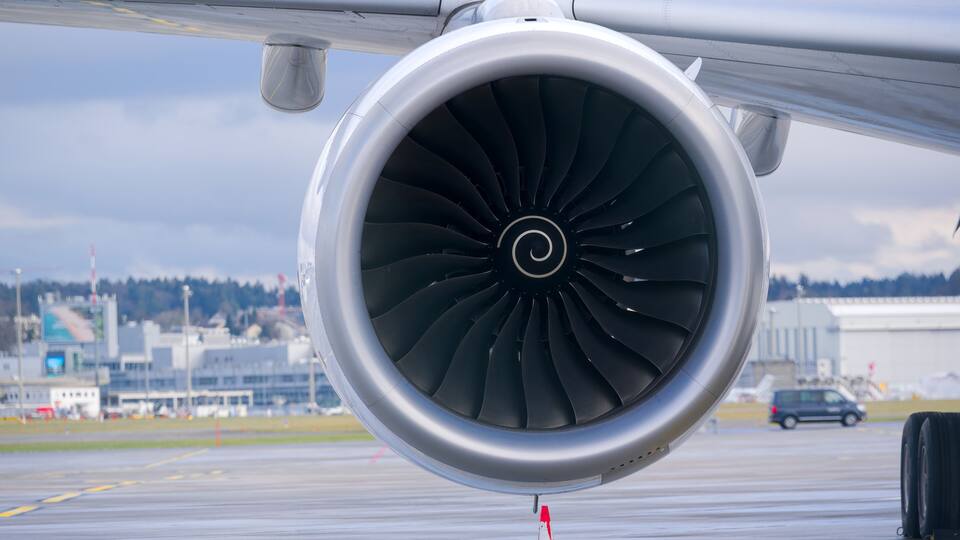 An airplane engine on a runway with a distant airport and buildings.