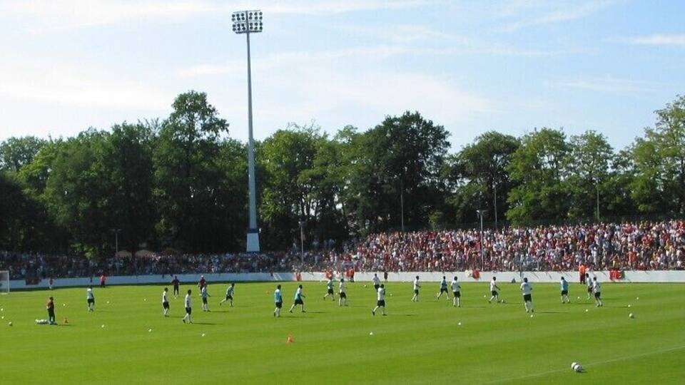 A soccer field with players, a goalpost, and a crowd in the background.
