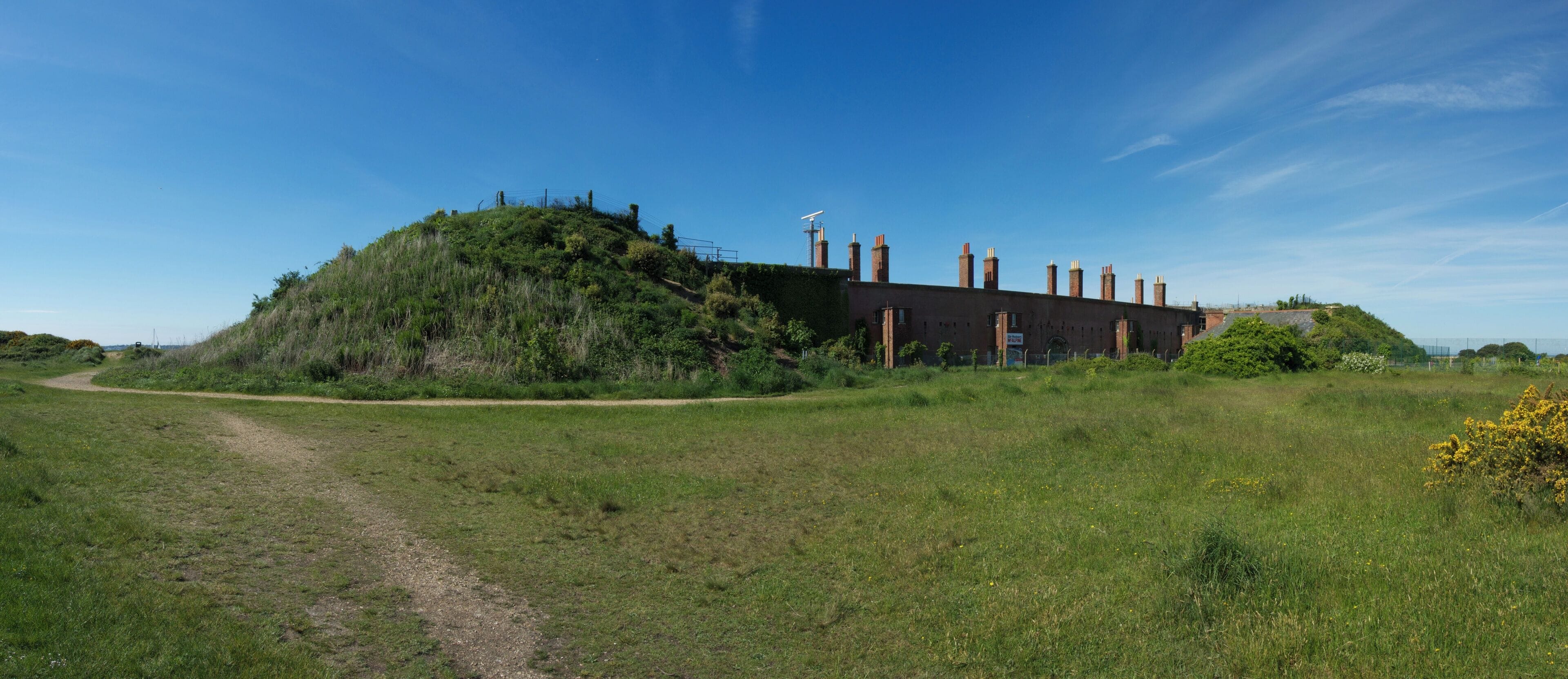 A grassy field with a dirt path leading to a large hill with a building on top.