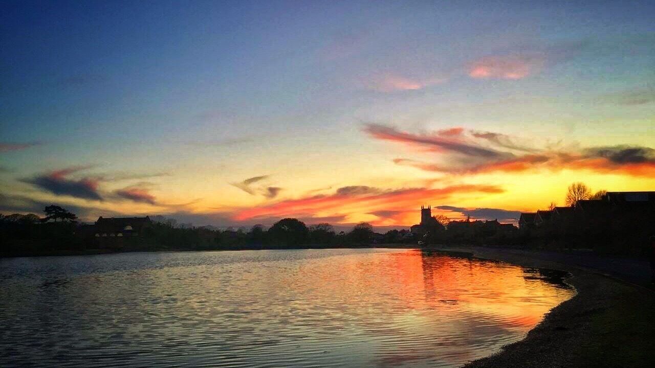 A sunset over a river with a silhouette of a castle and buildings on the horizon.