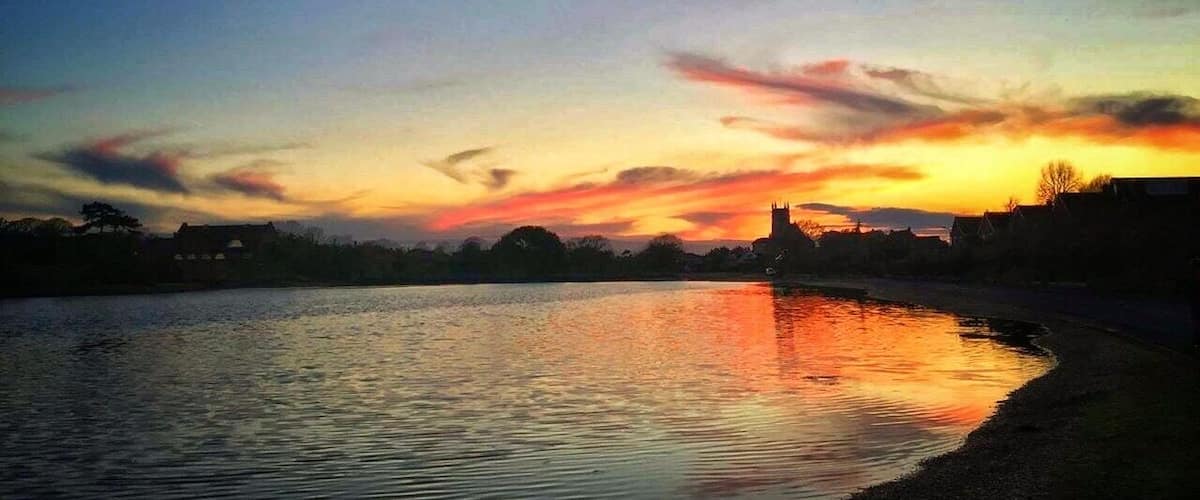 A sunset over a river with a silhouette of a castle and buildings on the horizon.