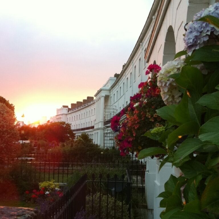 A sunset over a classical building with a garden in the foreground.