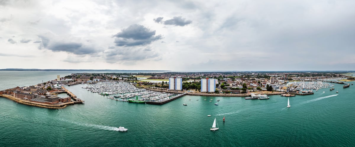 A coastal cityscape with a marina, historic buildings, and a large body of water.