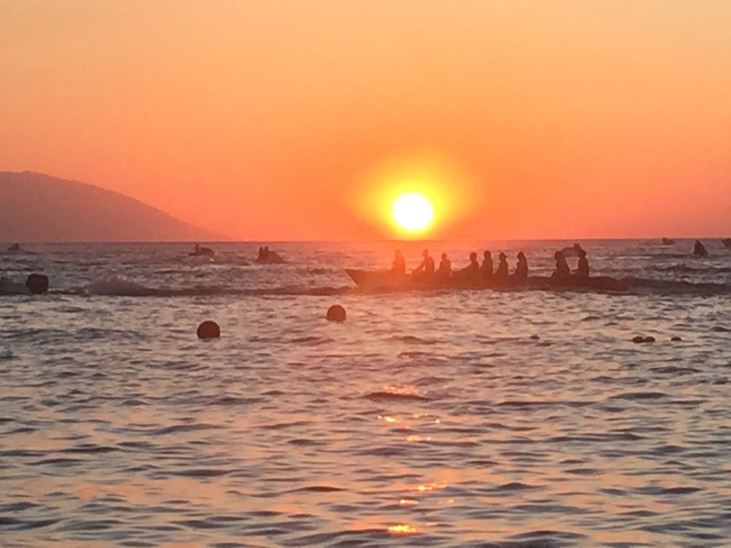 A sunset over the ocean with a group of people in a boat.