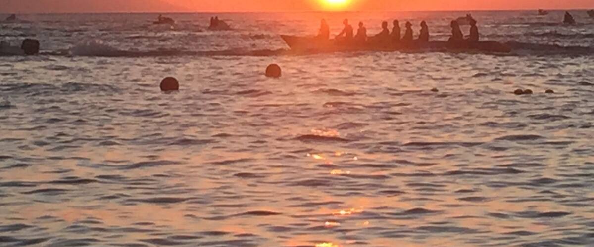 A sunset over the ocean with a group of people in a boat.