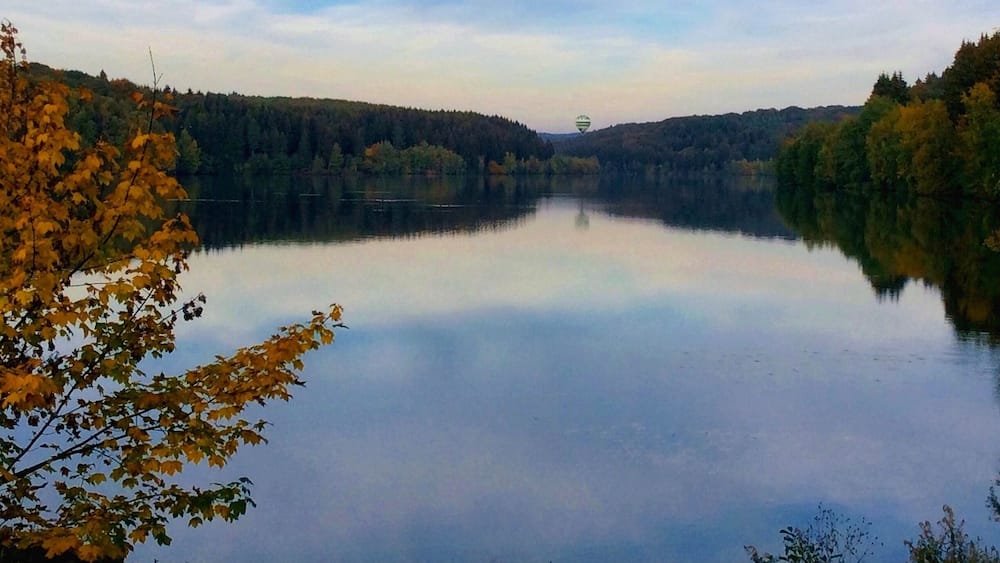 Ein ruhiger See, umgeben von herbstlich gefärbten Bäumen und einem klaren Himmel.
