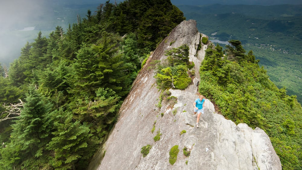 A woman trail running along a rocky ridge in Grandfather Mountain State Park, Linville, North Carolina.