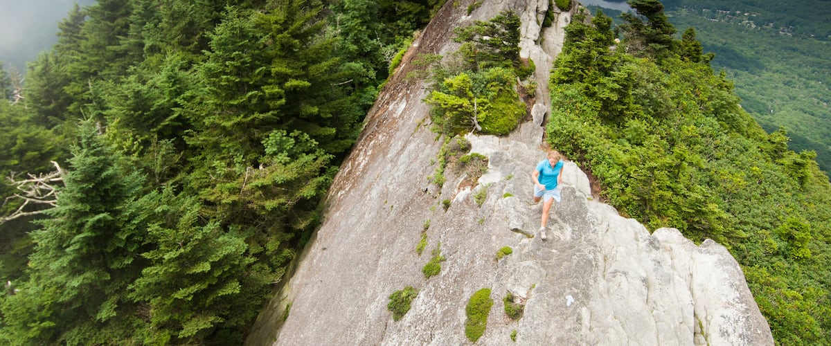 A person hiking on a rocky mountain ridge surrounded by dense forest.
