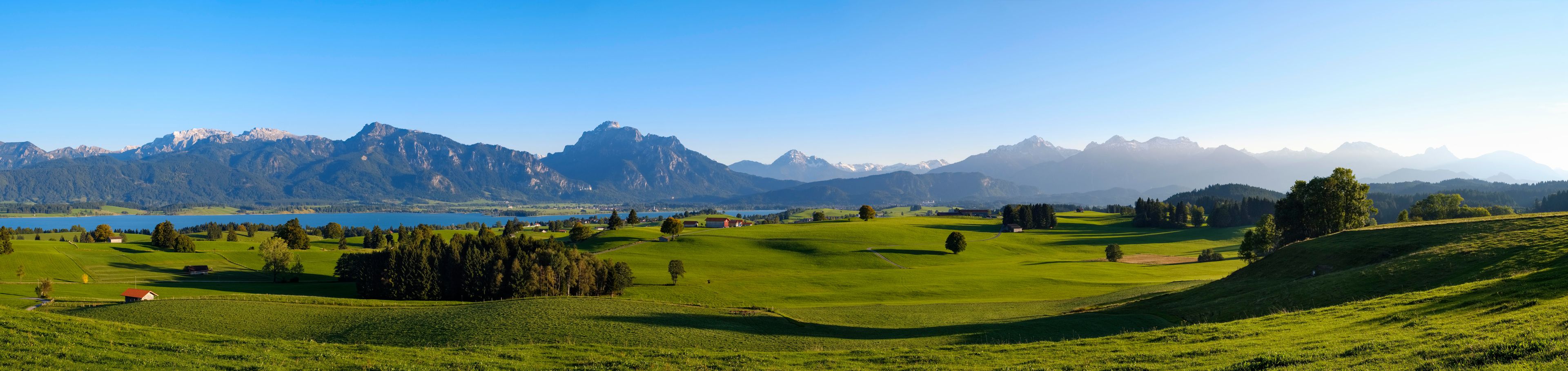 A green landscape with a lake, trees, and mountains in the background.