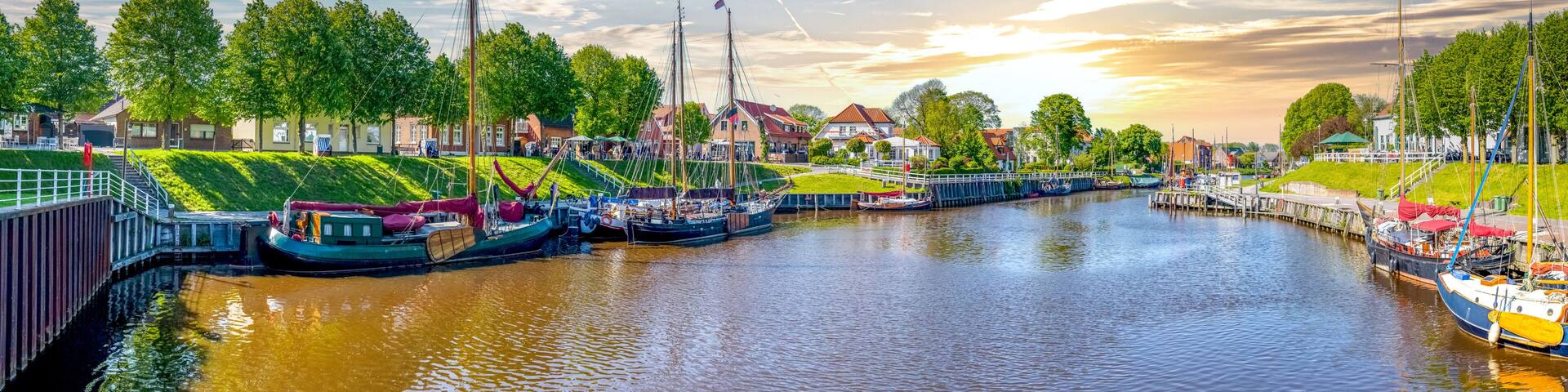 A canal lined with boats, a bridge, and houses with red roofs.