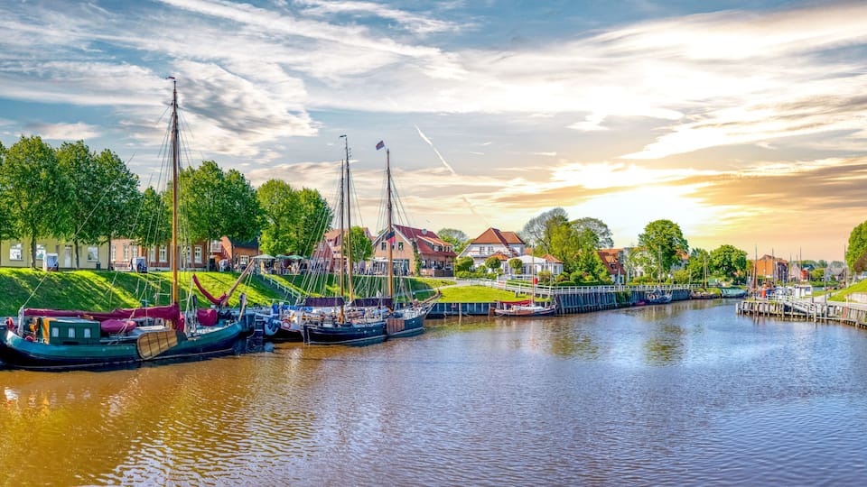 A canal lined with boats, a bridge, and houses with red roofs.