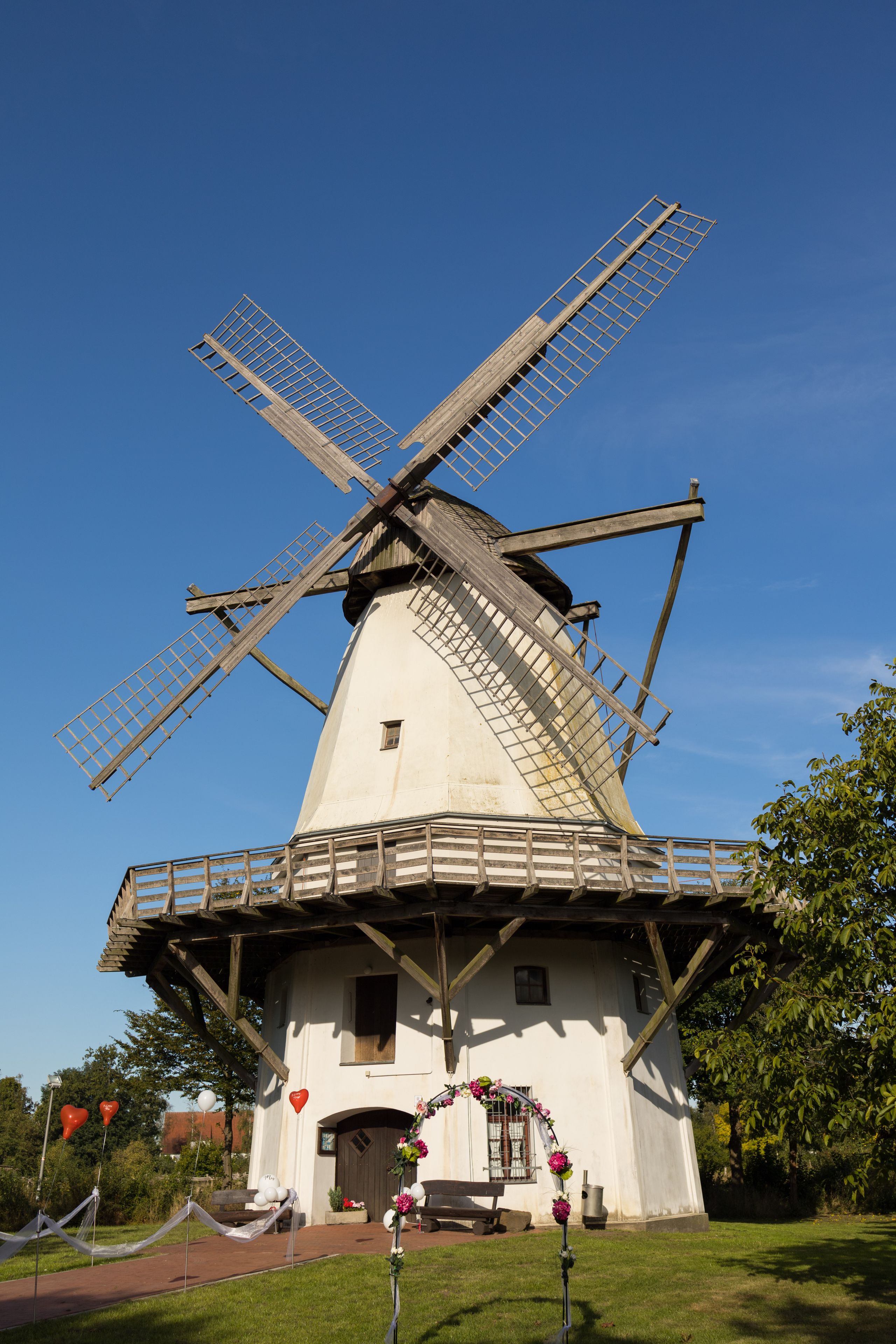 Een traditionele windmolen met een witte gevel en houten roerbladen, tegen een helderblauwe lucht.