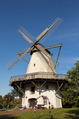 A traditional windmill with a white facade and wooden lattice blades, set against a clear blue sky.