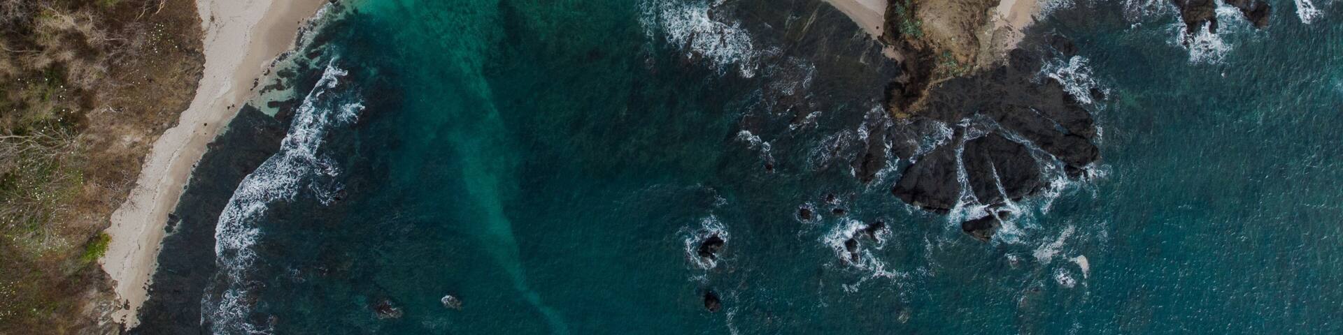 A coastal landscape with a sandy beach, clear turquoise waters, and rocky outcrops.