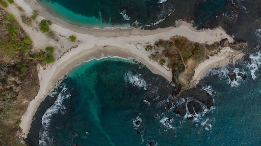 Un paisaje costero con una playa arenosa, aguas turquesas cristalinas y afloramientos rocosos.