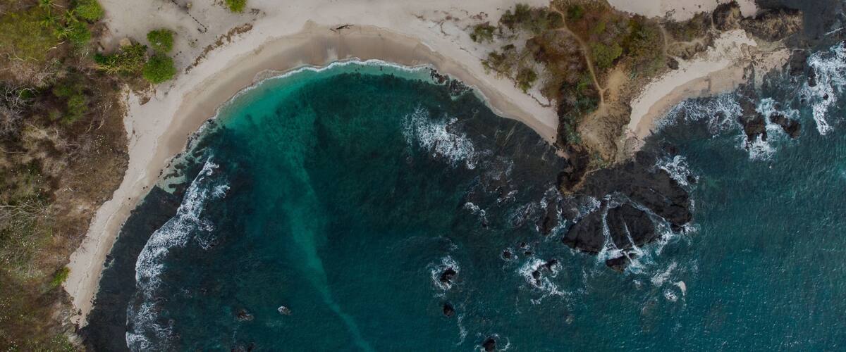 A coastal landscape with a sandy beach, clear turquoise waters, and rocky outcrops.
