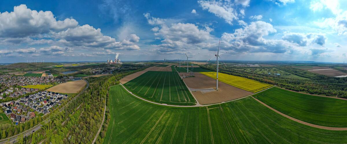 A rural landscape with wind turbines, fields, and a factory.