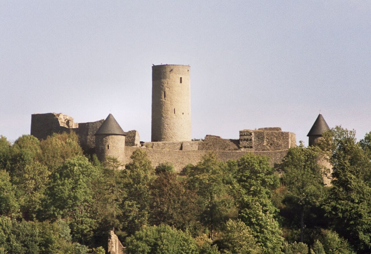 A medieval castle with a central tower, surrounded by trees and ruins.
