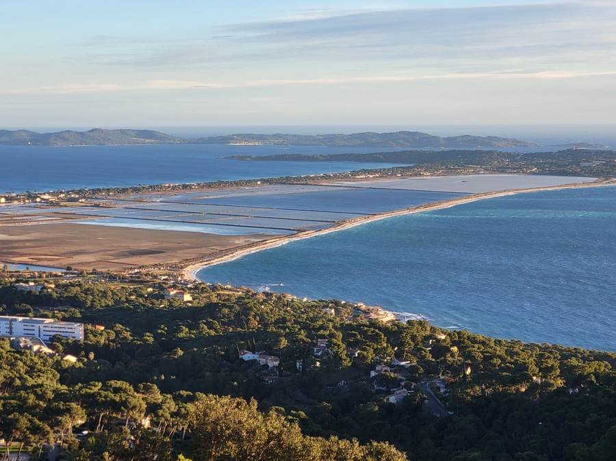 Un paysage côtier caractérisé par une ligne de rivage incurvée, un port de plaisance et une zone densément boisée parsemée de bâtiments.