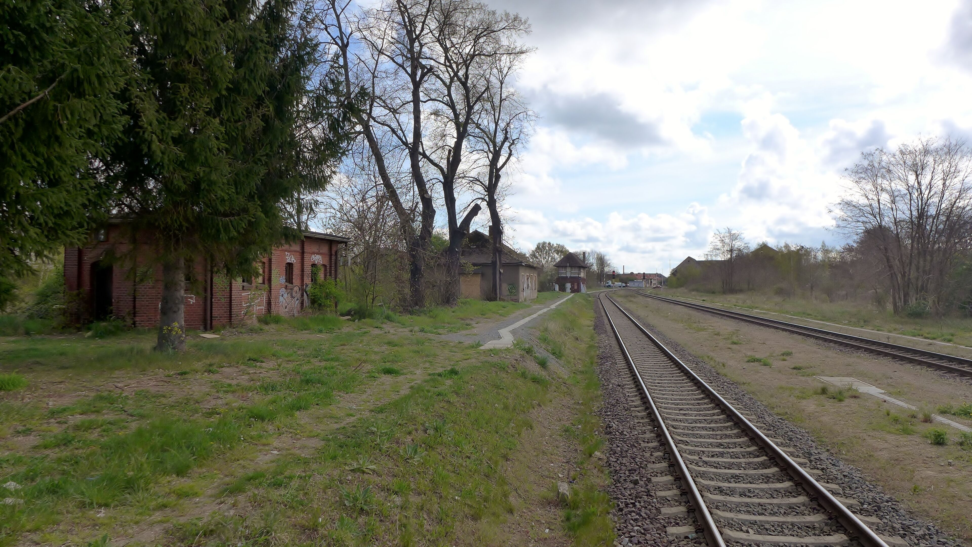 A railway track with a brick building and trees on the left.
