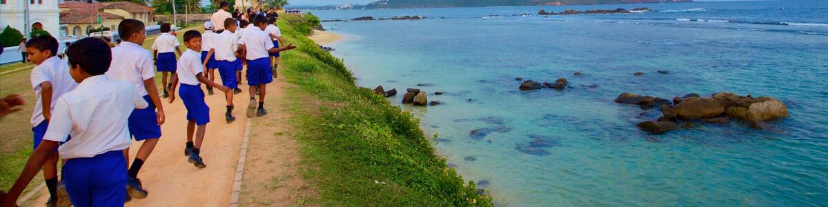 A coastal path with students in uniforms, a lighthouse, and rocky waters.