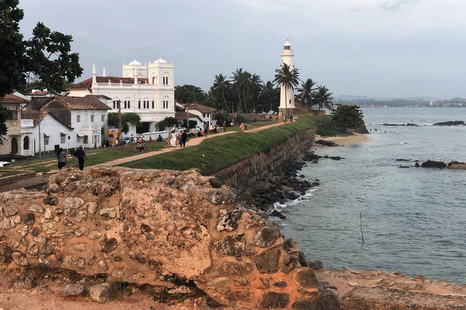 A coastal town with a prominent white church, a lighthouse, and a rocky shoreline.